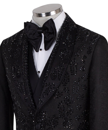 Front view of a black hand-embellished tuxedo with intricate beadwork and sequin patterns, displayed on a mannequin. Features a single-breasted jacket, peak lapel, matching vest, and trousers, embodying luxury bespoke craftsmanship from Istanbul.