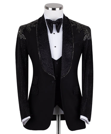 Black three-piece tuxedo on a mannequin, featuring a heavily hand-embellished shawl lapel, shoulders, and sleeves with intricate sparkling beadwork. The tuxedo includes a matching black vest and trousers, designed in a slim fit style, showcasing luxurious craftsmanship from Istanbul.