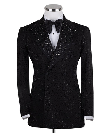 Close-up of a black double-breasted tuxedo jacket on a mannequin, showcasing intricate hand-embellishments with beads and crystals on the lapels and body. Features a peak lapel and black buttons, paired with a white shirt and black bow tie. Front view showing the full jacket and details.