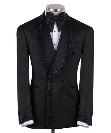 Front view of a black textured double-breasted tuxedo with hand-embellished shawl lapels, cuffs, and front trim. The trousers have a satin side stripe. High-end luxury formal wear from BTS Bespoke.