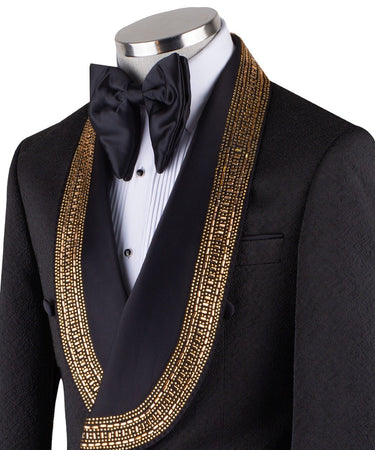 Mannequin wearing a black double-breasted tuxedo with ornate gold beaded peak lapels and matching cuff embellishments, paired with black satin-striped trousers.