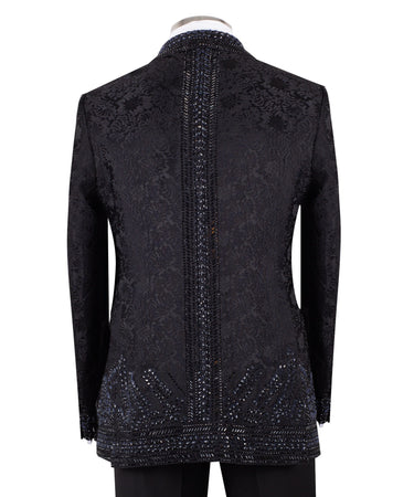 Front view of a luxurious black embellished jacquard double-breasted tuxedo jacket with intricate sequin and bead work on lapels, body, and sleeves, paired with black trousers, worn on a mannequin. From BTS Bespoke, handcrafted in Istanbul.