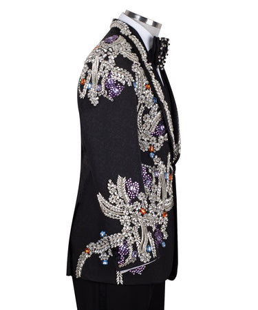 Front and side view of a black tuxedo jacket with extensive silver, purple, orange, and blue crystal and gemstone embellishments in floral and baroque patterns, paired with matching black trousers and vest, on a mannequin. Showcases intricate hand-embellished details and luxurious craftsmanship from BTS Bespoke, Istanbul.