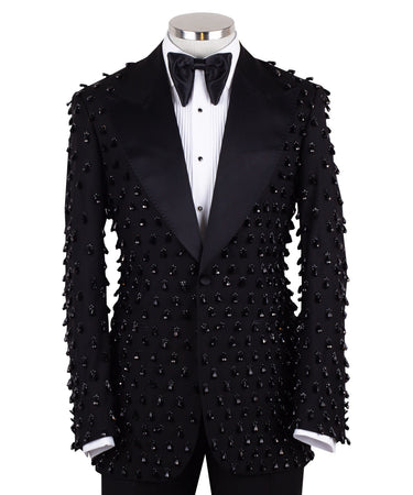Front view of a black hand-embellished luxury tuxedo jacket with satin peak lapels and matching trousers on a mannequin. Side view close-up of the jacket's intricate black bead embellishments. Close-up of the tuxedo trousers with a satin side stripe and high-waisted detail.