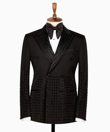 Front view of a black double-breasted tuxedo jacket featuring intricate hand-embellished studs on the peak lapels, shoulders, sleeves, and lower body, styled with matching black trousers with a satin side stripe. Handcrafted luxury from BTS Bespoke Istanbul.