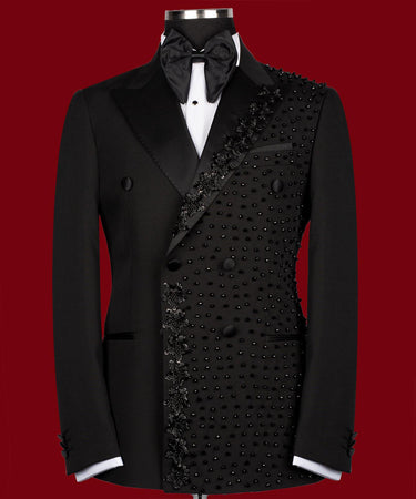 Front view of a black double-breasted tuxedo jacket with satin peak lapels and intricate hand-embellished black beading on the right side. Paired with matching trousers featuring a satin side stripe. High-end bespoke formal wear, handcrafted in Istanbul.