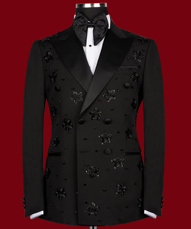 Front view of a black double-breasted tuxedo with satin peak lapels, adorned with intricate black beaded starburst embellishments, worn by a mannequin. The matching trousers with satin side stripe are also shown. This luxurious evening wear is handcrafted in Istanbul by BTS Bespoke.