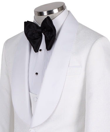 Front view of a white jacquard patterned single-breasted tuxedo jacket with a white satin shawl lapel, displayed on a mannequin. Includes a matching white jacquard vest and black trousers. Handmade in Istanbul luxury bespoke menswear.