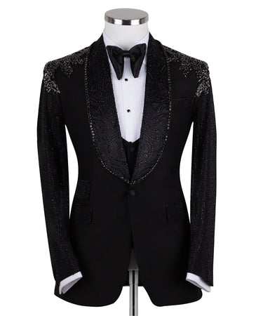 Black three-piece tuxedo on a mannequin, featuring a heavily hand-embellished shawl lapel, shoulders, and sleeves with intricate sparkling beadwork. The tuxedo includes a matching black vest and trousers, designed in a slim fit style, showcasing luxurious craftsmanship from Istanbul.