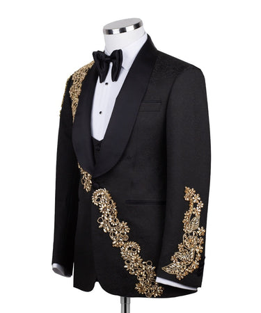 Front view of a black jacquard three-piece tuxedo with intricate gold hand-embellishments on the shawl lapel, shoulder, and cuffs, displayed on a mannequin. From BTS Bespoke, handcrafted in Istanbul.