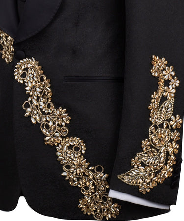 Front view of a black jacquard three-piece tuxedo with intricate gold hand-embellishments on the shawl lapel, shoulder, and cuffs, displayed on a mannequin. From BTS Bespoke, handcrafted in Istanbul.