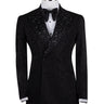 Close-up of a black double-breasted tuxedo jacket on a mannequin, showcasing intricate hand-embellishments with beads and crystals on the lapels and body. Features a peak lapel and black buttons, paired with a white shirt and black bow tie. Front view showing the full jacket and details.