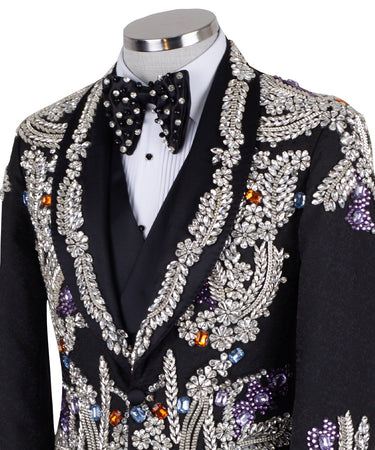 Front and side view of a black tuxedo jacket with extensive silver, purple, orange, and blue crystal and gemstone embellishments in floral and baroque patterns, paired with matching black trousers and vest, on a mannequin. Showcases intricate hand-embellished details and luxurious craftsmanship from BTS Bespoke, Istanbul.