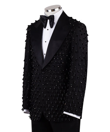 Front view of a black hand-embellished luxury tuxedo jacket with satin peak lapels and matching trousers on a mannequin. Side view close-up of the jacket's intricate black bead embellishments. Close-up of the tuxedo trousers with a satin side stripe and high-waisted detail.