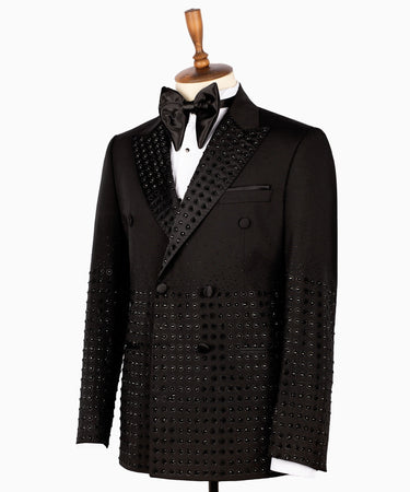 Front view of a black double-breasted tuxedo jacket featuring intricate hand-embellished studs on the peak lapels, shoulders, sleeves, and lower body, styled with matching black trousers with a satin side stripe. Handcrafted luxury from BTS Bespoke Istanbul.