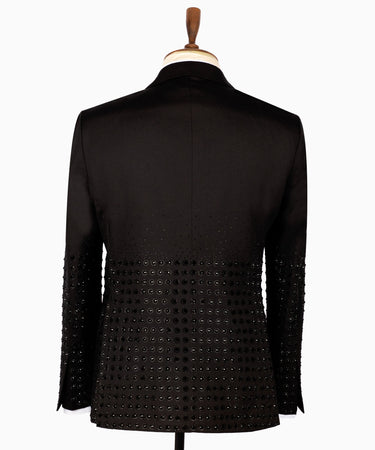 Front view of a black double-breasted tuxedo jacket featuring intricate hand-embellished studs on the peak lapels, shoulders, sleeves, and lower body, styled with matching black trousers with a satin side stripe. Handcrafted luxury from BTS Bespoke Istanbul.