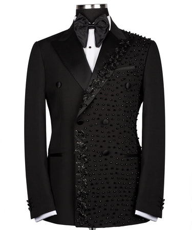 Front view of a black double-breasted tuxedo jacket with satin peak lapels and intricate hand-embellished black beading on the right side. Paired with matching trousers featuring a satin side stripe. High-end bespoke formal wear, handcrafted in Istanbul.