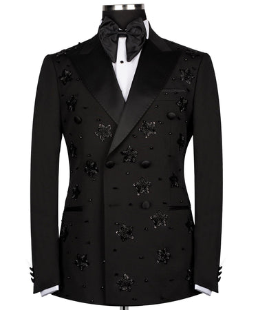 Front view of a black double-breasted tuxedo with satin peak lapels, adorned with intricate black beaded starburst embellishments, worn by a mannequin. The matching trousers with satin side stripe are also shown. This luxurious evening wear is handcrafted in Istanbul by BTS Bespoke.